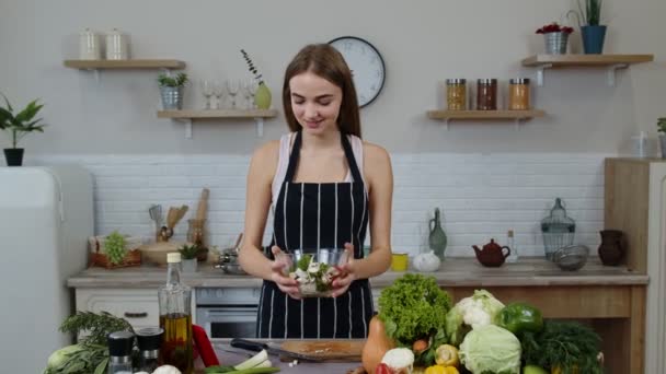 Sonriente joven comiendo ensalada de verduras crudas frescas posando en la cocina con emoción positiva — Vídeo de stock