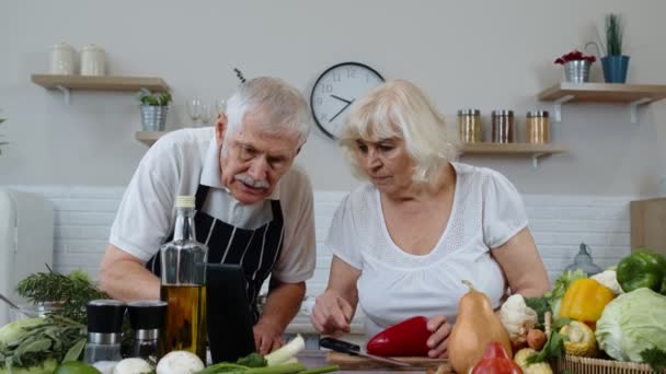 Веганская старшая пара готовит салат из сырых овощей. Глядя на цифровой планшет для онлайн рецепт — стоковое видео