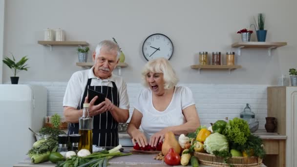 Старша пара готує салат з овочами. Жінка танцює, тримаючи свіжі скибочки перцю на очах — стокове відео