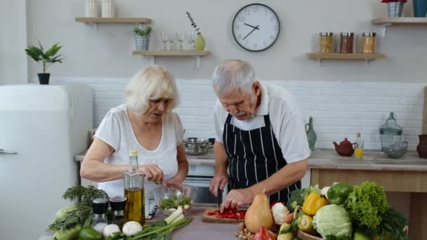 Abuela vegana senior y abuelo cocina ensalada con verduras frescas en la cocina en casa — Vídeos de Stock