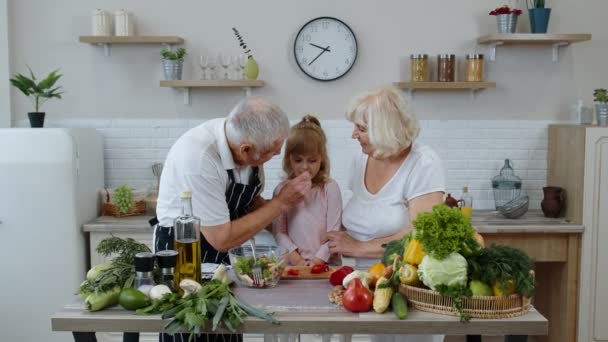 Starsi dziadkowie w kuchni karmią wnuczkę siekaną czerwoną papryką. Dieta wegetariańska — Wideo stockowe