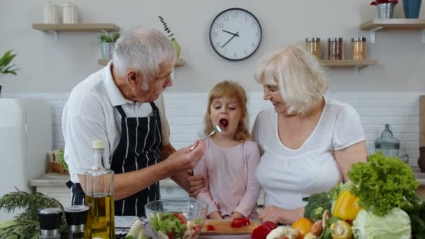 Ancianos abuelos en la cocina de alimentación nieto niña con pimiento rojo picado. Dieta vegetariana — Vídeos de Stock