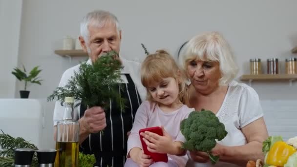 Blogcu torun kızı, mutfakta sebzeli büyük anne ve büyük babasıyla telefonda selfie çekiyor. — Stok video