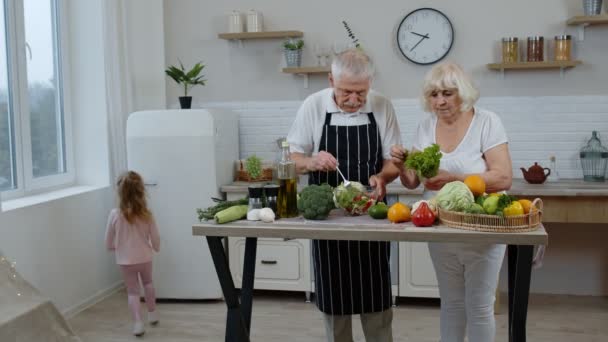 Starsza babcia i dziadek gotujący sałatkę. Wnuczka dająca warzywa z lodówki — Wideo stockowe