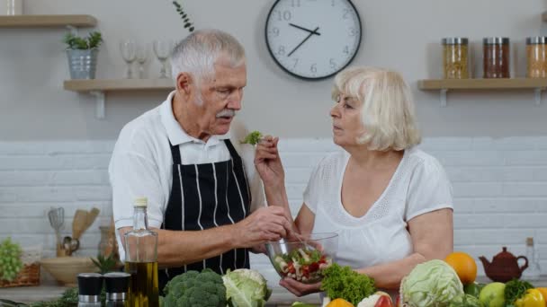 Casal sénior na cozinha. Avó e avô alimentando um ao outro com salada vegetal crua — Vídeo de Stock