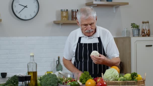 Oudere grootouders in keuken interieur. Senioren vrouw en man koken salade met verse groenten — Stockvideo