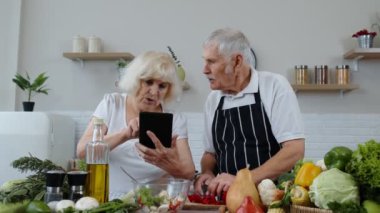 Vejetaryen büyük anne ve büyük baba dijital tablette yemek tarifi arıyor, salata pişiriyorlar.