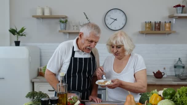 Een stel in de keuken. Grootmoeder voedt grootvader met rauwe kiemgroenten boekweit met noten — Stockvideo