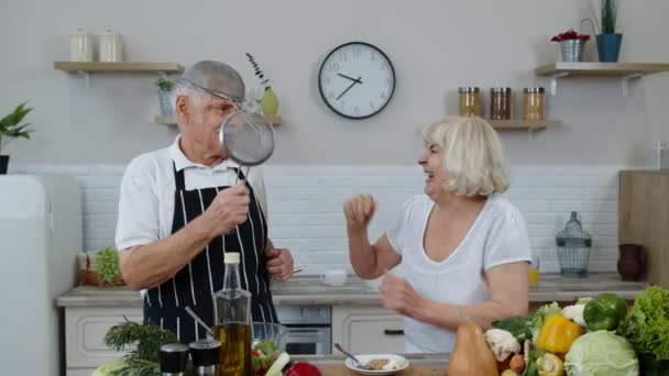 Mujer mayor y hombre haciendo un baile divertido con coladores. Bailando mientras cocinan juntos en la cocina — Vídeos de Stock