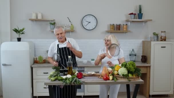 Femme âgée et homme faisant une danse drôle avec des passoires. Danse en cuisinant ensemble dans la cuisine — Video