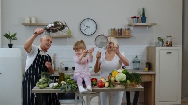 Мужчина и женщина старшего возраста с внучкой делают смешной танец со стрейнером и овощами дома — стоковое видео
