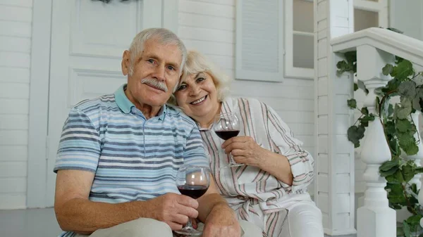 Пожилая пара пьет вино, обнимается дома на крыльце во время карантина коронавируса — стоковое фото