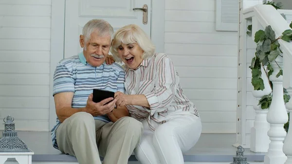 Senior elderly caucasian couple using digital tablet in porch at home. Enjoy online shopping, news