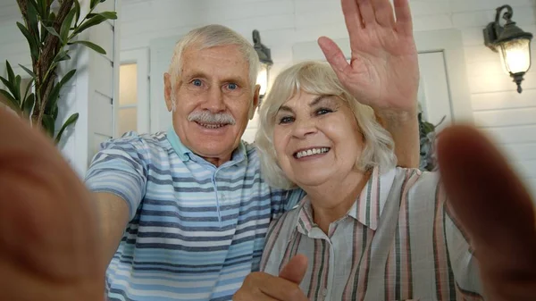 Старший мужчина, женщина делает селфи видео вызов, обнимает, смеется, машет руками, в крыльце дома — стоковое фото