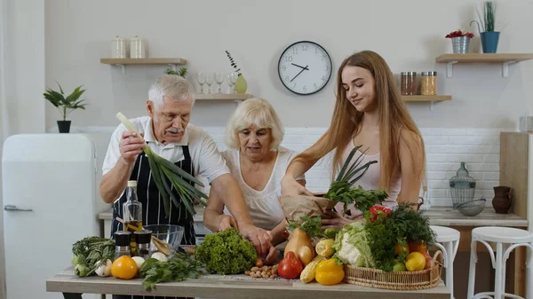 Elderly couple in kitchen receiving vegetables from grandchild. Raw food healthy eating diet