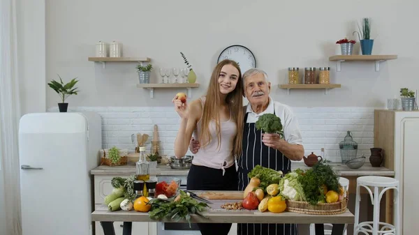 Uomo maturo con nipotina che consiglia di mangiare cibo vegetale crudo. Mondo vegan day concept — Foto Stock