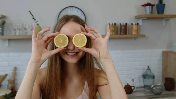 Joyful young girl vegan holding fresh halves of lemon on eyes and fooling around, making funny faces — Stock Photo, Image