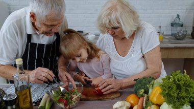 Mutfaktaki yaşlı büyükanne ve büyükbaba torununa salata pişirmeyi, kırmızı biber doğramayı öğretiyor.