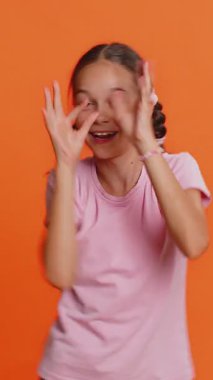 Neşeli, komik, genç, sevimli kız kameraya surat asıyor, şakalaşıyor, aptal suratıyla maymun taklidi yapıyor, alay ediyor. Turuncu arka planda 10 yaşında küçük bir çocuk. Küçük çocuklar