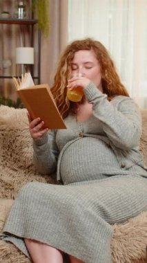 Hamile genç bir kadın evde kanepede oturmuş taze portakal suyu yudumluyor ve rahat bir ifadeyle hamilelik kitabı okuyor. Geleceğin anneliğini ve nazik yaşam tarzını yansıtan mutlu anları seven bir kız.