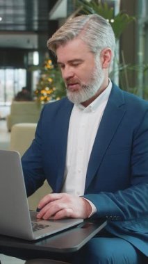 Modern ofis lobisinde oturan Kafkasyalı mutlu iş adamı işi bitirdikten sonra dizüstü bilgisayarı kapatıp kollarını uzatıyor. İnternette çalışan, e-öğrenen, internette gezinen takım elbiseli adam..