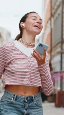 Kablosuz kulaklıklı mutlu, gevşemiş yetişkin kız dışarıda dans eden enerjik disko rock n roll müziği dinliyor. Beyaz bir kadın yaz caddesinde yürüyor..