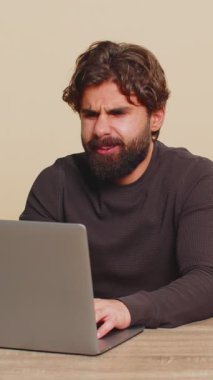 Masa başında dizüstü bilgisayar kullanan genç Hintli adam yazı işlerinde çalışırken, aniden piyango sonuçları, kötü haberler, servet kaybı, başarısızlık şaşkınlığını kaybediyor. Yakışıklı Hindu adam bej renkli stüdyo arka planında izole edilmiş..