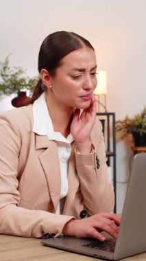 Ev işlerindeki genç iş kadını dizüstü bilgisayarla çalışıyor yanaklarına dokunuyor, diş ağrısı çekiyor ve kaşlarını çatıyor. Masadaki serbest çalışan kız, işe dönmeden önce yanaklarını ovuşturuyor ve işine devam ediyor.