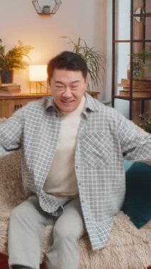 Dertsiz orta yaşlı Çinli adam evinde oturma odasında kafasının arkasında kanepede rahatça oturuyor. Gülümseyen Koreli erkek kanepede dinleniyor. Daire odasına bakıyor..