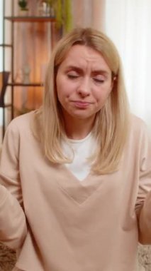 Genç yetişkin bir kadın evdeki kanepede otururken elini sallayarak internetten gelen olumsuz mesaja tepki veriyor. Sarışın kız hayal kırıklığı, anlaşmazlık, duygusal protesto ve hoşnutsuzluk gösteriyor.