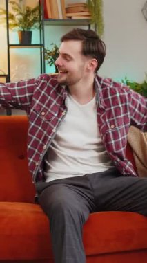 Oturma odasında kanepede otururken elleri ile şarkı söyleyip dans eden enerjik genç adam. Tasasız Kafkasyalı adam zaferi kutluyor favori müziğin tadını çıkarıyor evde tek başına eğlenirken..