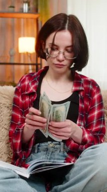 Genç bir kadın, aile bütçesini dikkatli bir şekilde defterine yazıp, ciddi şekilde odaklanmış bir şekilde parayı sayıyor. Kız parayı sorumlulukla yönetiyor, ev giderlerini kontrol ediyor ve düzenli kalıyor..