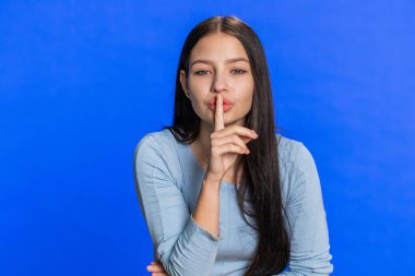 Sessiz olun lütfen. Genç bir kadın işaret parmağını dudaklarına bastırıyor sessizlik işareti yapıyor. Gizli saklı konuşmayın, dedikoduyu kesin. Oldukça çekici esmer bir kız mavi stüdyo arka planında tek başına.