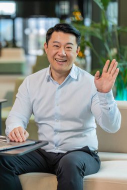 Hoş geldiniz. Mutlu Çinli işadamı el sallayarak selam veriyor. Birine hoş geldin diyor. İnternet ağları, uzaktan konuşma. Modern ofis lobisinde oturan gömlekli girişimci adam..