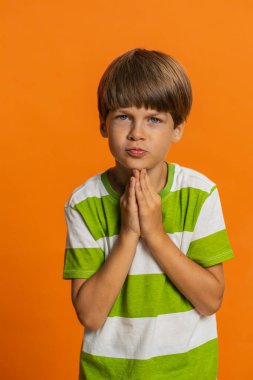 Lütfen, Tanrım yardım et. Ergen çocuk dua ediyor, dilek diliyor, umutlu bir şekilde yalvarıyor, özür diliyor, kötü davranışları için onu cezalandırmamayı diliyor. Turuncu arka planda küçük çocuklar