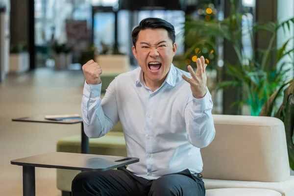 Tişörtlü kızgın yetişkin patron ofisteki modern işyerindeki kameraya bakarak video konuşması yapıyor. Tatminsiz Çinli iş adamı, şirket sorunları hakkında astlarıyla iletişim kuruyor..