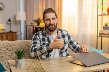 Mutlu gülümseyen genç adam ev masasındaki görevlerini tamamlıyor, bilgisayarını minnettar bir ifadeyle kapatıyor. Kanepede oturan beyaz bir adam kameraya doğru dönüyor, iyi bir iş çıkardığını söylüyor..