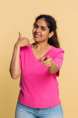 Hintli kadın formları bana jest der. Elini kulağının yanına koyar, parlak bir şekilde gülümser. Bej arka plandaki Hindu kız mutlu bir şekilde telefon görüşmesi, iletişim, sohbet ya da dostça bir temas öneriyor..