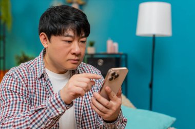 Kanepede oturan Asyalı adam akıllı telefondan internet formunu dolduruyor. Dikkatlice ekrana dokunuyor ve ciddi bakışlar atıyor. Çinli adam dijital uygulama sırasında hataları önlemek için özenli konsantrasyon gösteriyor.