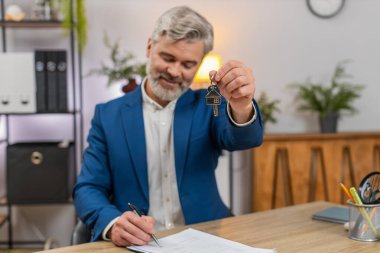 Merkez ofisteki orta yaşlı işadamı, kira kontratının üstündeki dairenin anahtarlarını gururla gösteriyor. Masadaki serbest çalışan adam kira onayını ve yaklaşan hamleyi kutluyor..