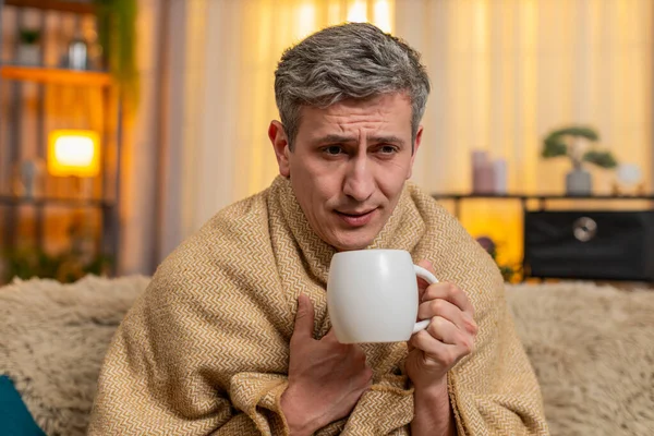 Evdeki üzgün genç adam bir fincan çayla battaniyeye sarılmış, hasta görünüyor ve öksürüyor. Kanepedeki beyaz adam soğuk algınlığı belirtileri gösteriyor, sessizce dinleniyor ve hafif bir hastalık ve yorgunluktan kurtulmaya çalışıyor.