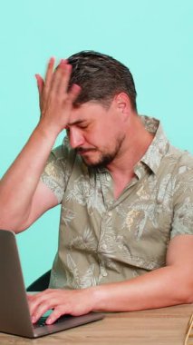 Orta yaşlı bir adam masada oturmuş, kötü haberler alıyor, dizüstü bilgisayarında yenilgiye uğruyor ve hayal kırıklığını açıkça gösteriyor. Genç, yetişkin bir adam mavi arka planda izole edilmiş. Sinirli.