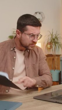 İnternetteki dizüstü bilgisayar aramasında tartışan üzgün işadamı ev ofis masasında rapor çizelgeleri ve grafikler gösteriyor. Genç adam bilgisayar araması sırasında agresif bir şekilde konuşuyor. Stresli serbest çalışan. Tartışma!.