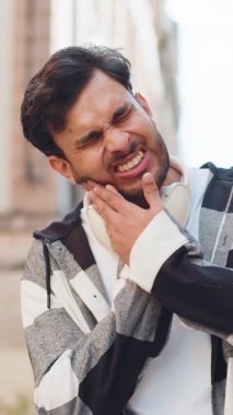 Üzgün, yetişkin bir genç adam şehir caddesinde dururken diş ağrısı çekiyor. Acı çeken üzgün Hintli erkek turist. El ele tutuşup masaj yapıyor. Bir dişçinin yardımına ihtiyacı var..