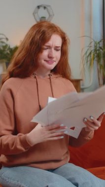 İş çizelgelerini ve grafikleri inceleyen ve ödenmemiş faturaları evdeki oturma odasındaki kanepede oturarak havaya atan, stresli, Kafkasyalı genç kadın. Kızgın kızıl saçlı uzaktan kumandalı kız koltukta çalışıyor..