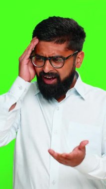 Hintli bir adam eline facepalm jesti göstererek alnına tokat atar, açık bir hata üzerine hayal kırıklığını ifade eder. Yeşil krom anahtar arka planında izole edilmiş Arap adam duygusal farkındalık gösteriyor