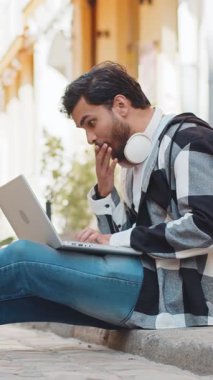 Laptop kullanan yakışıklı İspanyol genç adam iyi haber kazanıyor, piyango zaferi kazanıyor, açık havada internetten dağıtıyor. Şehir caddesinde oturan mutlu Hintli turist. Kasaba yaşam tarzları