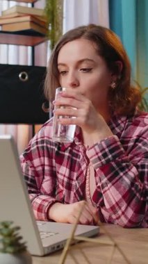 İşyerindeki masasında oturup laptopla çalışırken su içen Kafkasyalı iş kadını kız. Kadın serbest çalışan kadın bilgisayar ekranı internette geziniyor..