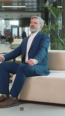 Kafkasyalı işadamı, modern ofis lobisindeki başarı zaferini kutladıktan sonra kanepeye yaslanıyor. Mutlu sakallı, takım elbiseli bir erkek otel odasında ellerini başının arkasına koyuyor..