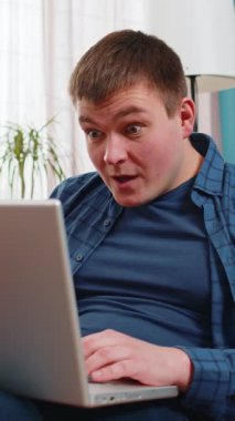 Laptop bilgisayar kullanan beyaz bir adam, iyi haber mesajı alıyor, evdeki kanepede piyango kazanma ikramiyesini kutlayan ani zaferi kutluyor. Yaşam Tarzları.